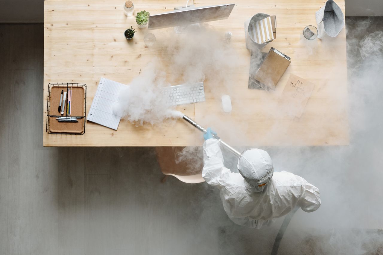services-01 An individual disinfects a workspace using fumigation, wearing full protective gear for safety.