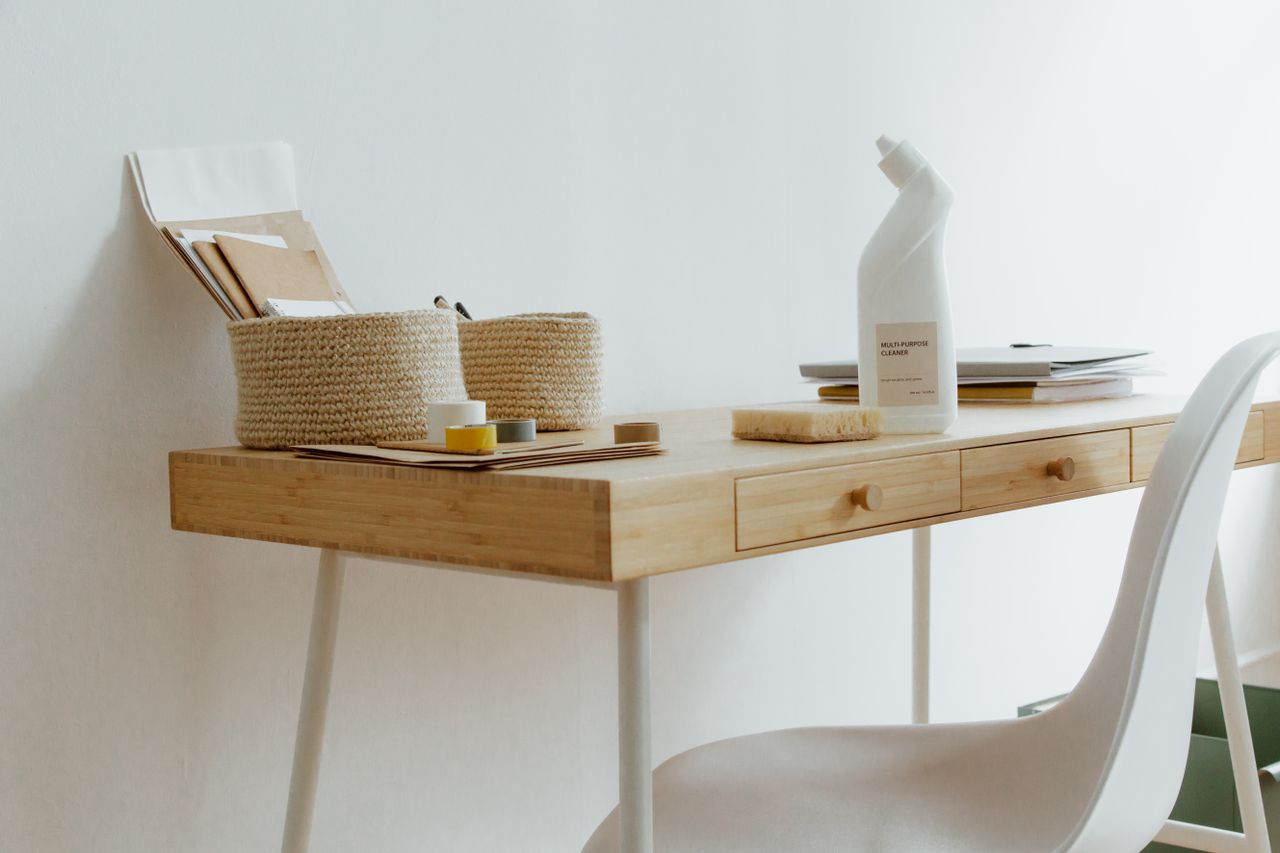 team-02 A clean and organized home office desk with cleaning products, papers, and storage baskets.